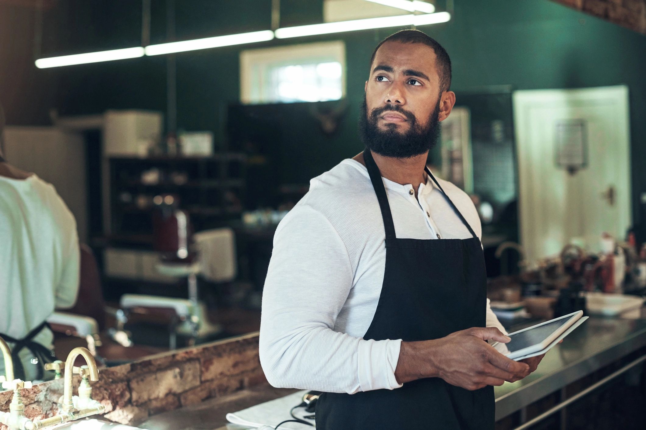 Barber in apron holding a phone inside a barber shop.