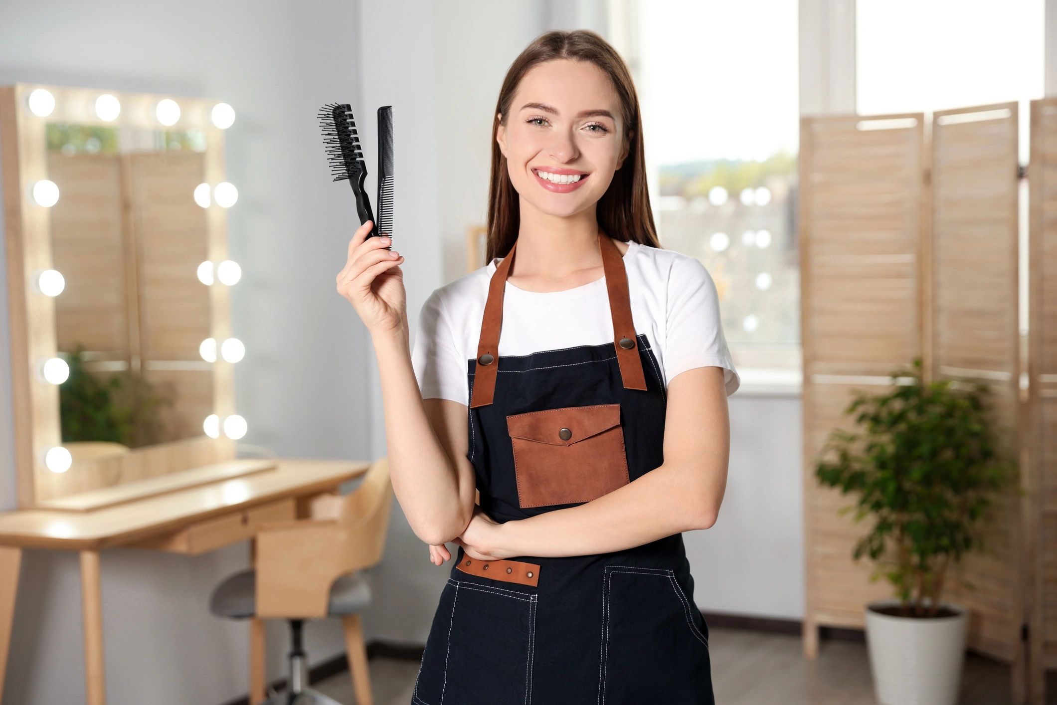 Smiling hairstylist holding hair straighteners in salon.