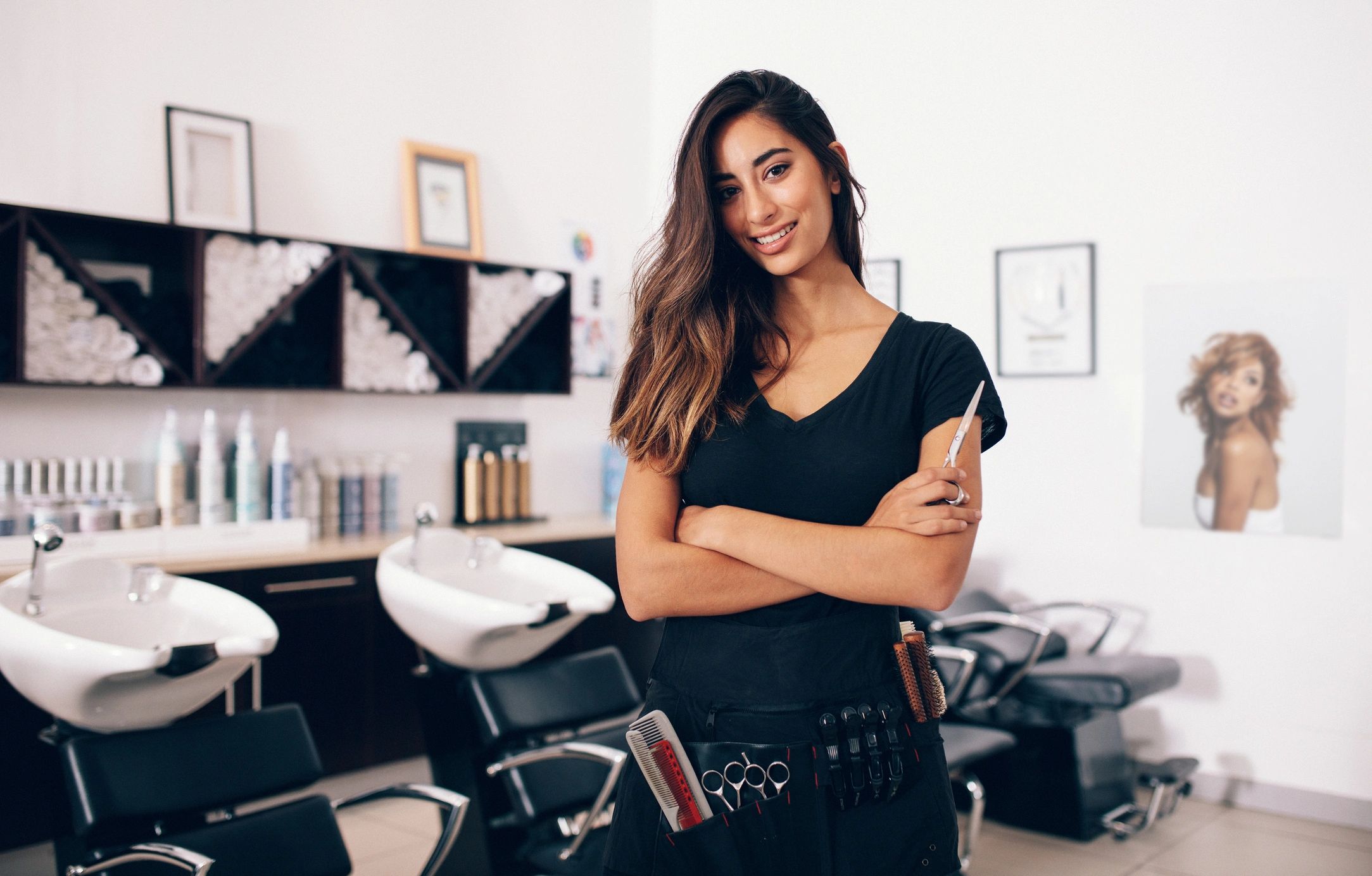 Confident hairstylist standing in a modern salon with arms crossed.